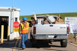A man in a hardhat and high visibility vest inspects a pickup truck loaded with junk