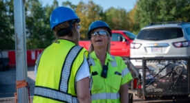 Two women wearing high visibility yellow vests and blue hard hats conversing joyfully