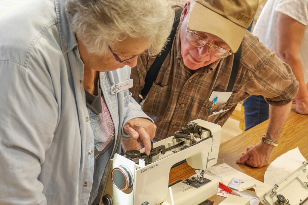 Two people leaning over a sewing machine, pointing and looking at its inner workings.