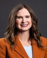 A headshot of a Caucasian woman with wavy brown hair and hazel eyes.