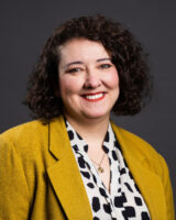 A headshot of a Caucasian woman with curly, dark brown hair and brown eyes.